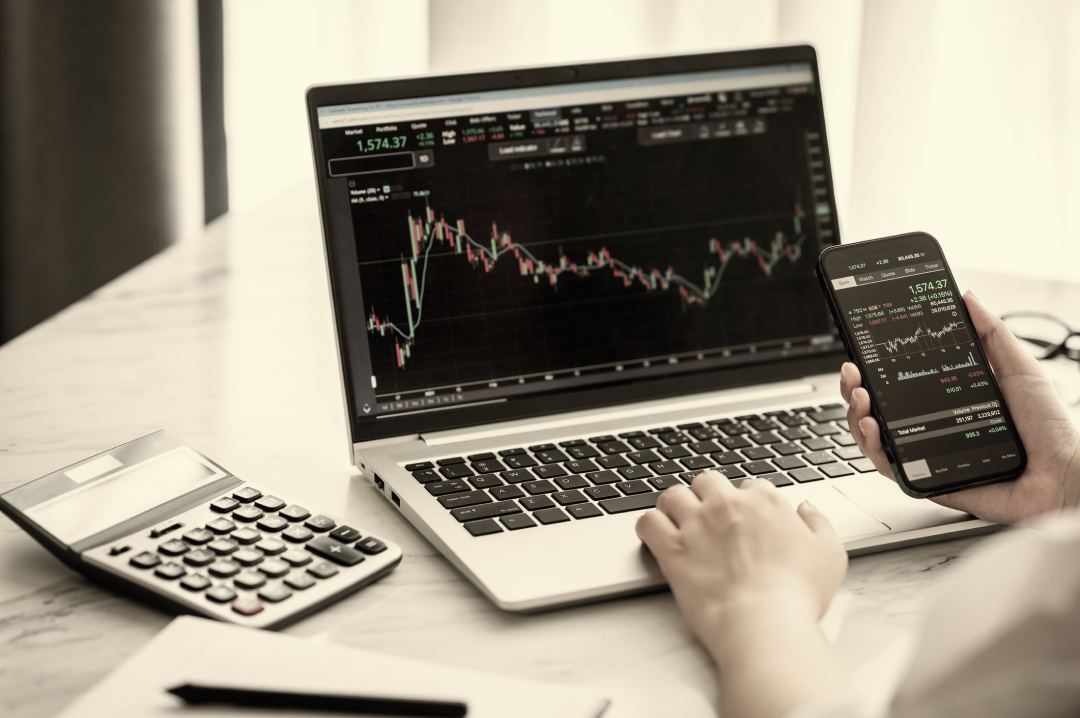 A work station where someone is viewing stocks on their phone and laptop. 